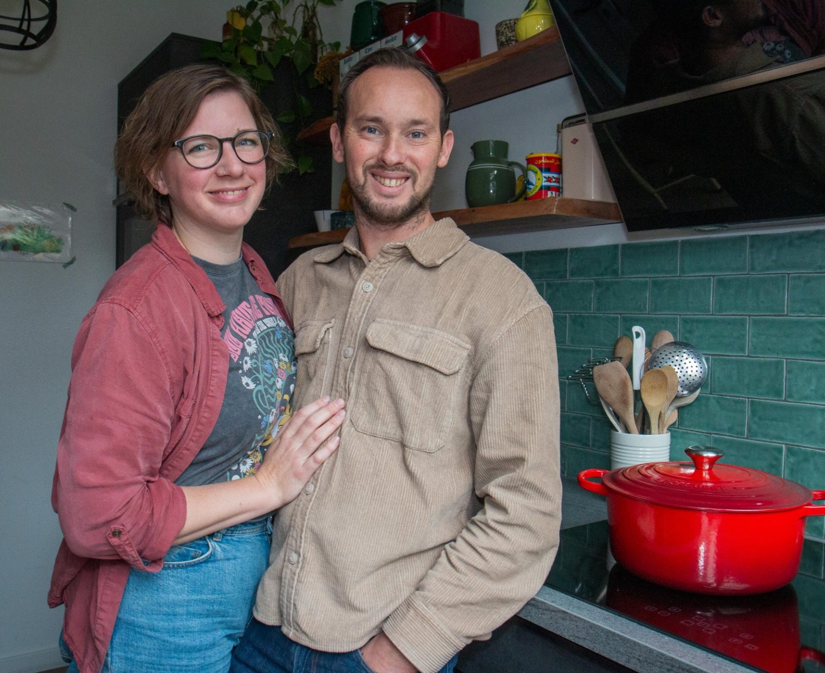 personen Een stel poseert samen in een modern ingerichte keuken met rode kookpot.